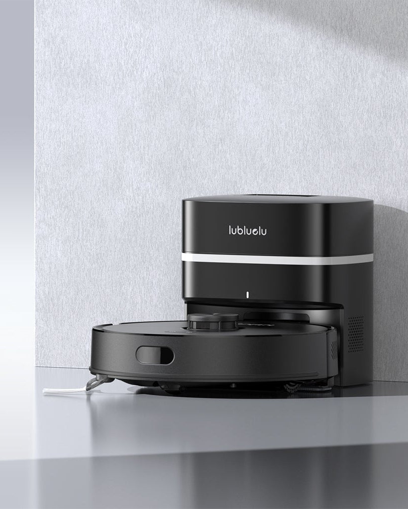 A black robotic vacuum cleaner and its matching charging dock on a light gray surface against a textured gray wall, with promotional text reading 'L50 Max' and a 'Learn More' button on the left.